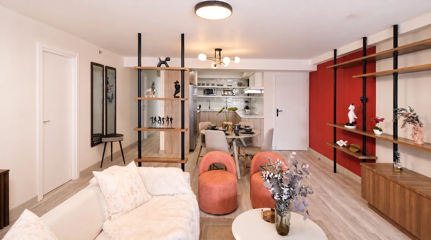 Sala con sillones coral, pared roja y cocina al fondo